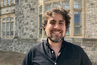 Geoff Adelsberg, wearing a collared shirt, stands in front of the Hokie Stone of Burruss Hall. 
