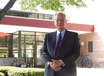 Scott Midkiff wearing suit and tie standing outdoors in front of class atrium of building