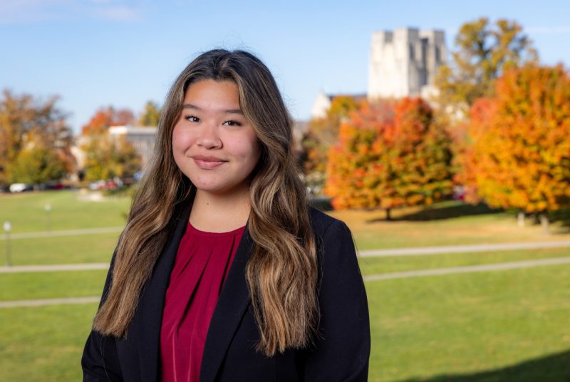 Dani Villarroel smiles wearing a blouse and business jacket with fall foliage and Burruss Hall behind her.