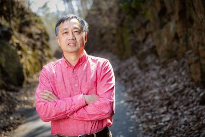 Shuhai Xiao stands with his arms crossed outside, wearing a button-down shirt.