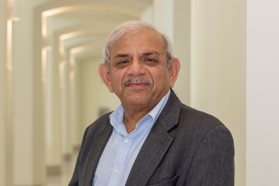 Portrait of Raman Kumar wearing a suit and standing in a hallway.