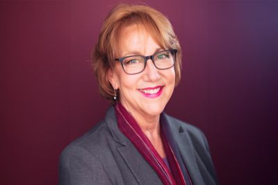 Headshot of Patty Raun in a business suit, smiling in front of a blank photo backdrop.