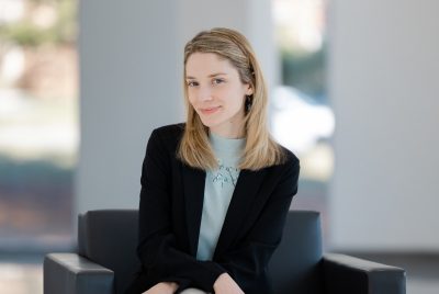 Headshot of Eleanor Webster wearing a business jacket and sitting in a chair in front of a window.