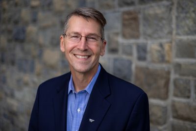 Headshot of Mark Owczarski in a suit and standing in front of a wall of Hokie Stone.