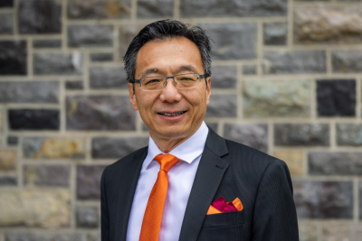 Portrait shot of Lu Liu in suit with Hokie colors, standing in front of a Hokie Stone wall.