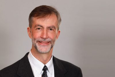 Portrait of Robin McCarley, smiling for a photo, wearing a black suit. 