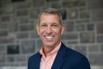 Headshot of Dwyn Taylor smiling in a suit in front of a wall of Hokie Stone.