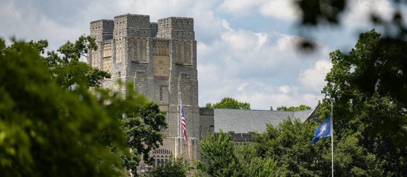  Burruss Hall seen through the trees with the American and Virginia flags in front.